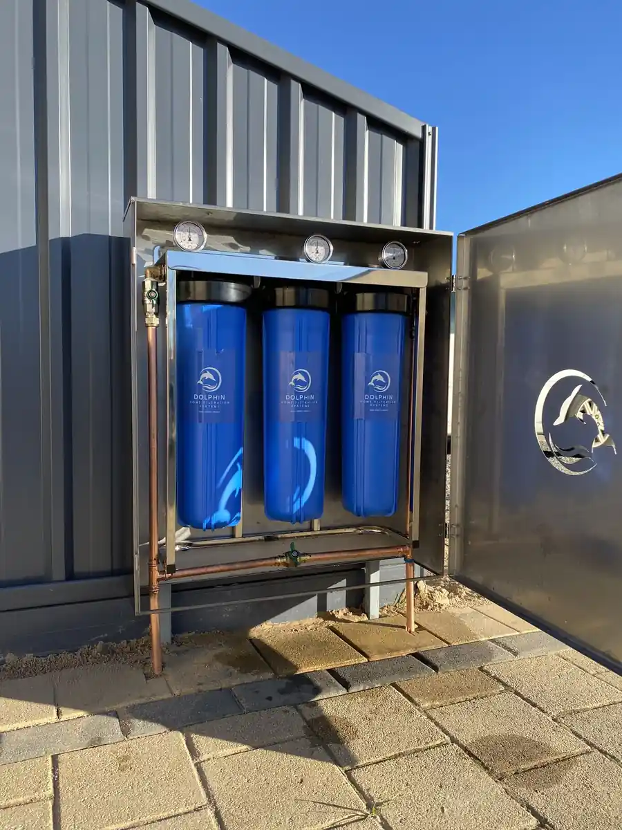 Dolphin whole-house filtration unit installed outdoors with the stainless enclosure open, showing three filter housings